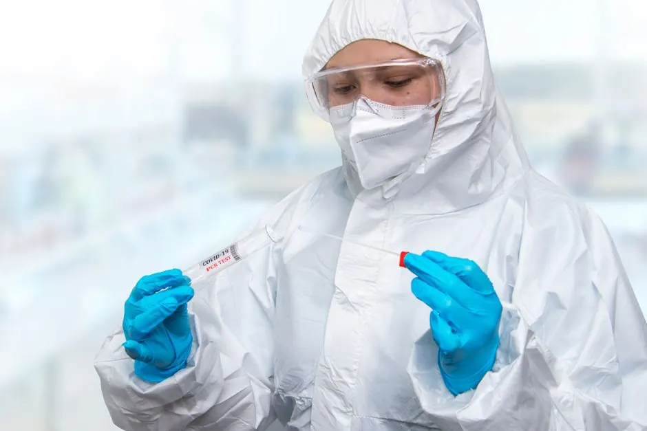 A medical professional in full protective gear performing a COVID-19 test indoors.