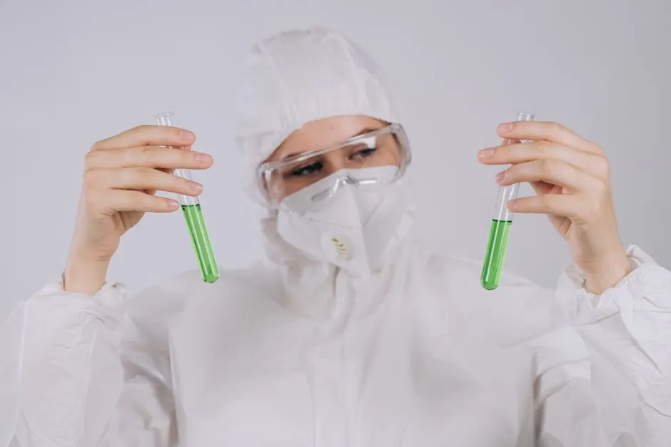 A scientist in protective gear observing green liquids in test tubes, demonstrating laboratory safety.